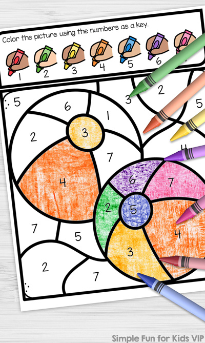 Picture of the Beach Ball Color by Number Coloring Page on top of a white desk. The image is partially colored in and crayons in 7 colors are scattered on top of the paper. There's a Simple Fun for Kids VIP watermark in the bottom right corner.